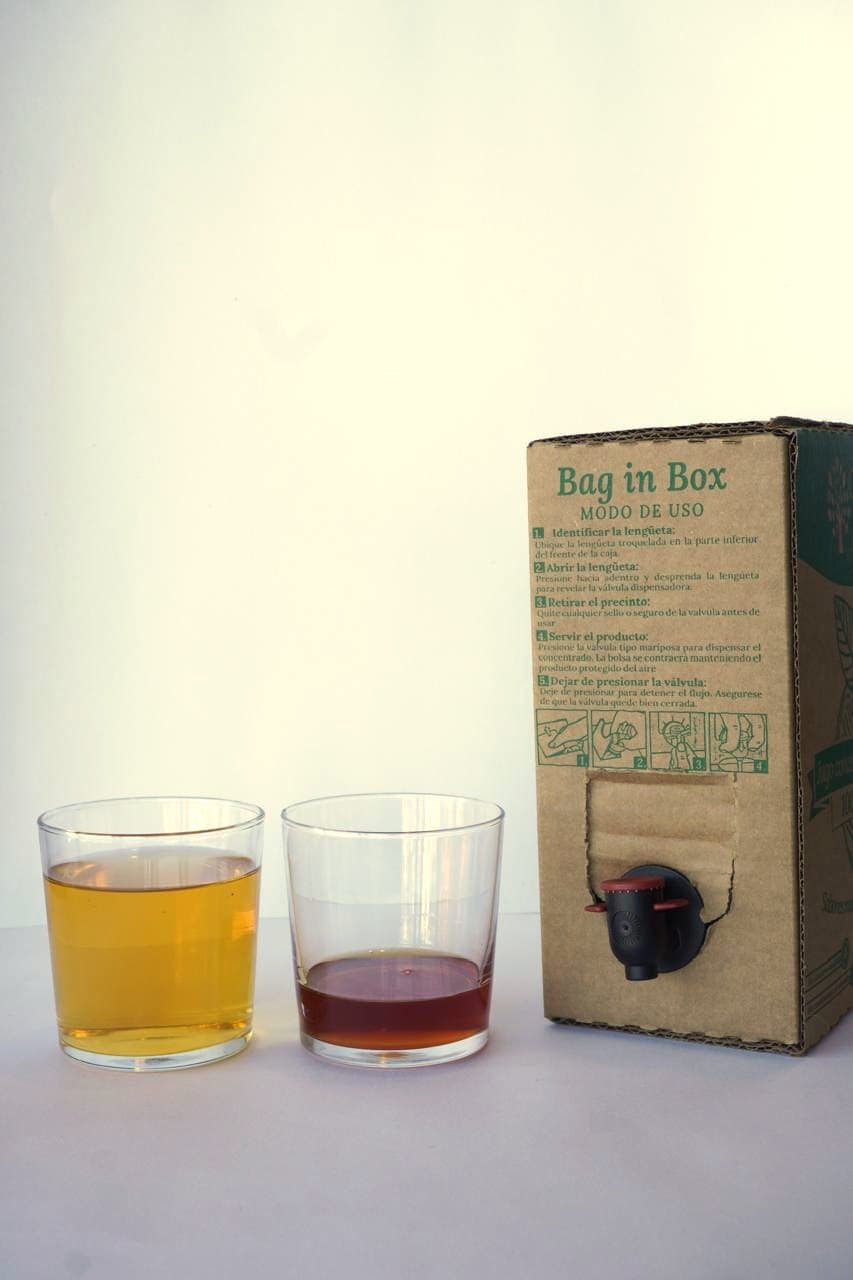 Dos vasos lado a lado: uno con jugo de manzana ya diluido y otro con el concentrado sin diluir, junto a la caja Bag in Box