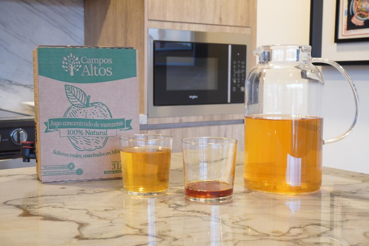 Caja Bag in Box de Campos Altos junto a una jarra de jugo de manzana servido y dos vasos, sobre una barra de cocina