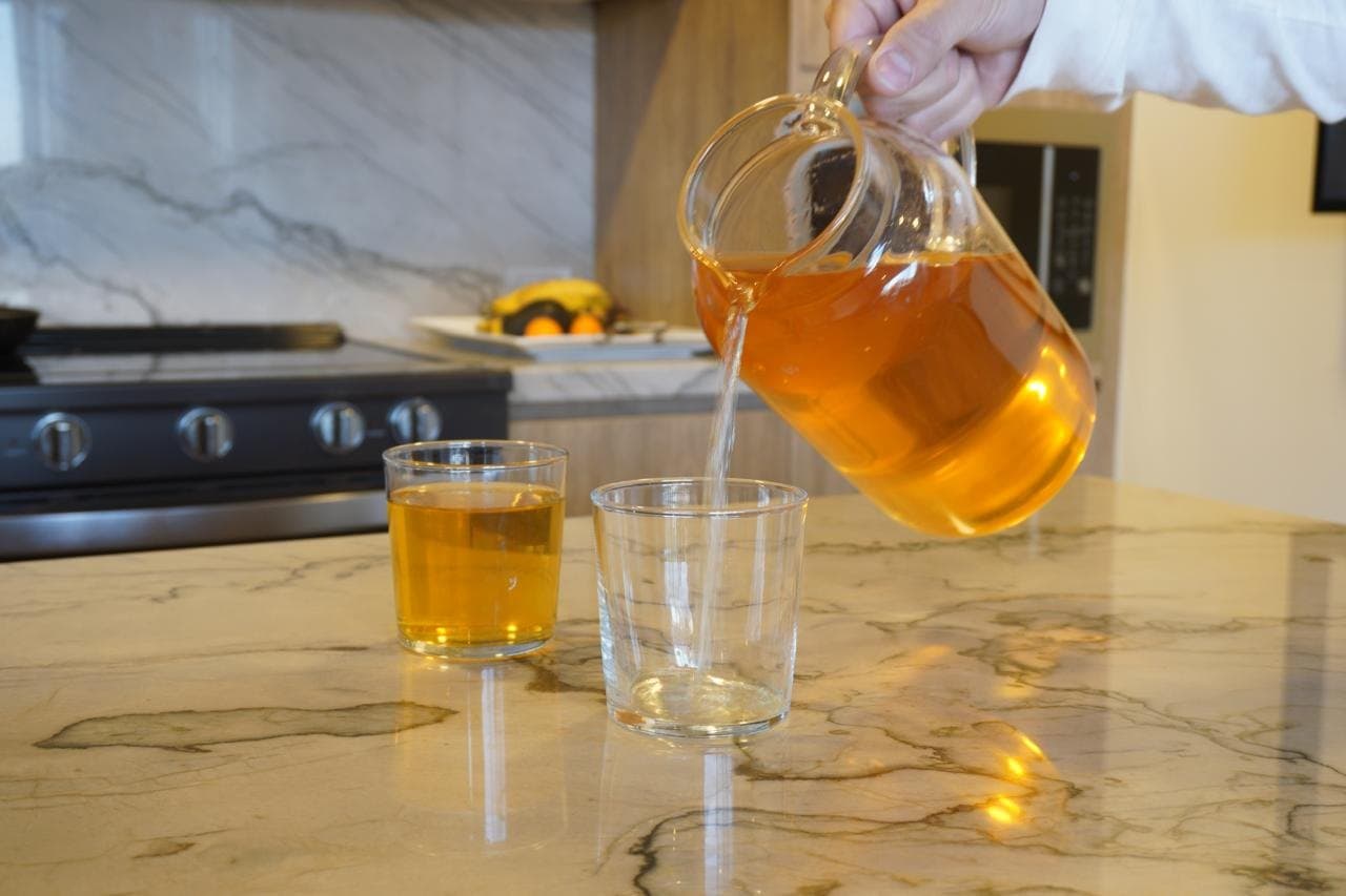 Jarra de vidrio sirviendo jugo de manzana en un vaso sobre una barra de cocina